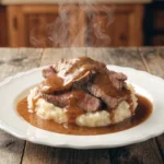 Thin sliced beef served over creamy mashed potatoes topped with rich brown gravy and steam rising on a rustic table