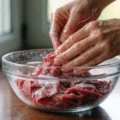 hands mixing thin sliced beef with baking soda for tenderizing in bowl