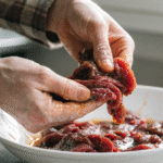 hands coating thin sliced beef with cornstarch and marinade for tender stir fry