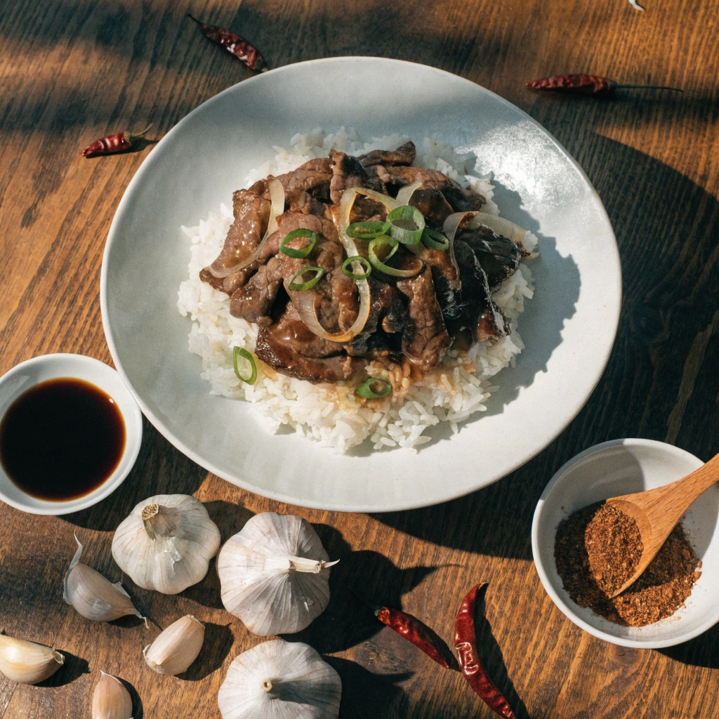 Thin sliced beef served over white rice with garlic, soy sauce, and spices on a wooden table