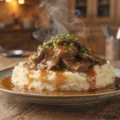 Tender thin sliced beef covered in rich brown gravy served over creamy mashed potatoes with steam rising